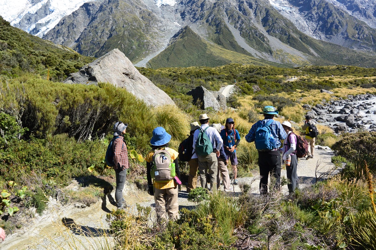 Hikers standing on an alpine trail below snowy New Zealand mountains