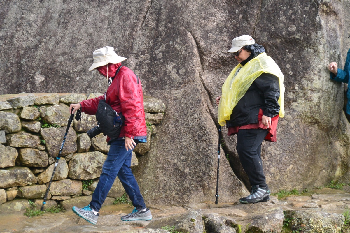Hikers in rain gear walking beside stone walls